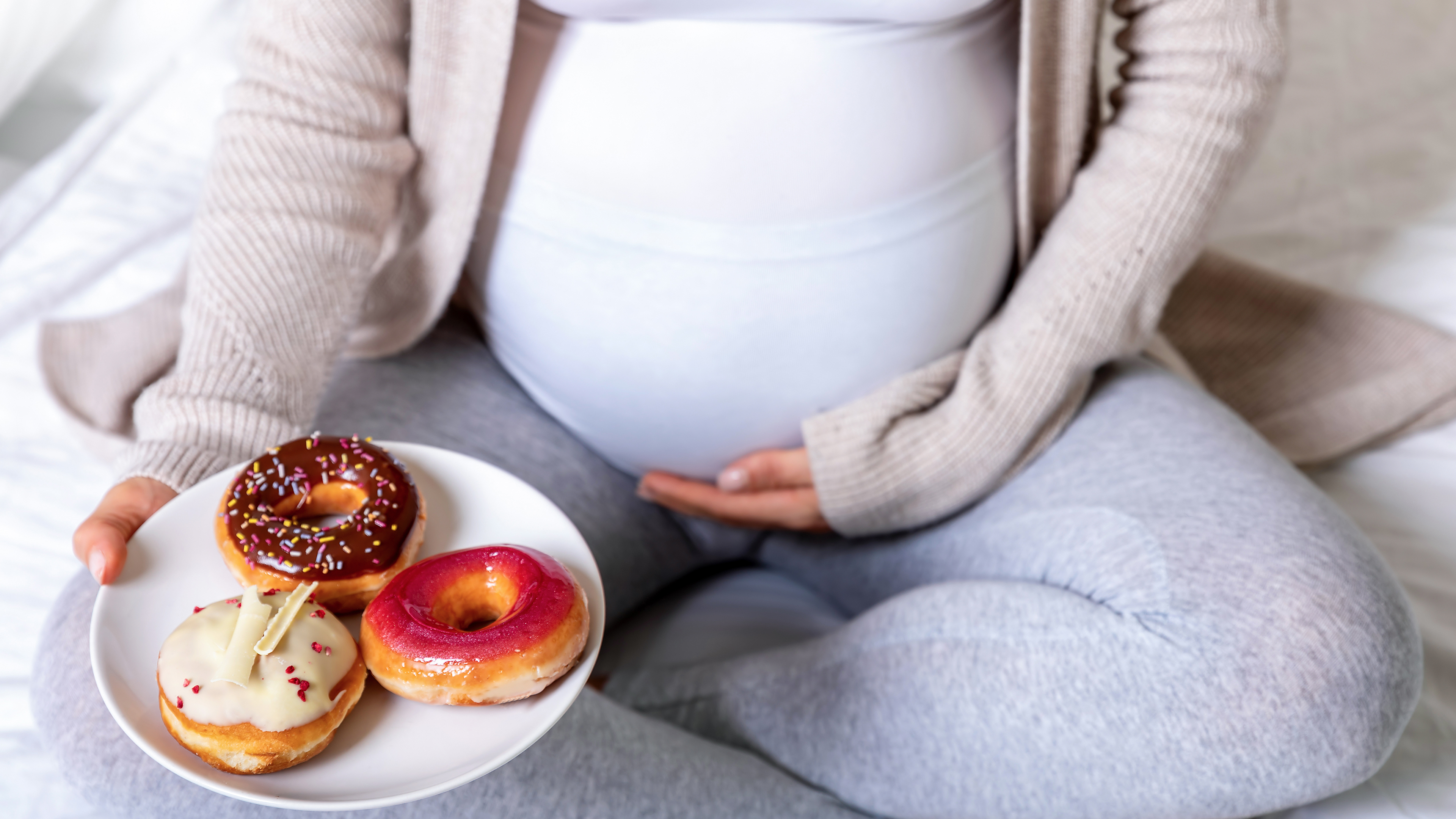 Pregnant woman holding her belly and a plate of donuts