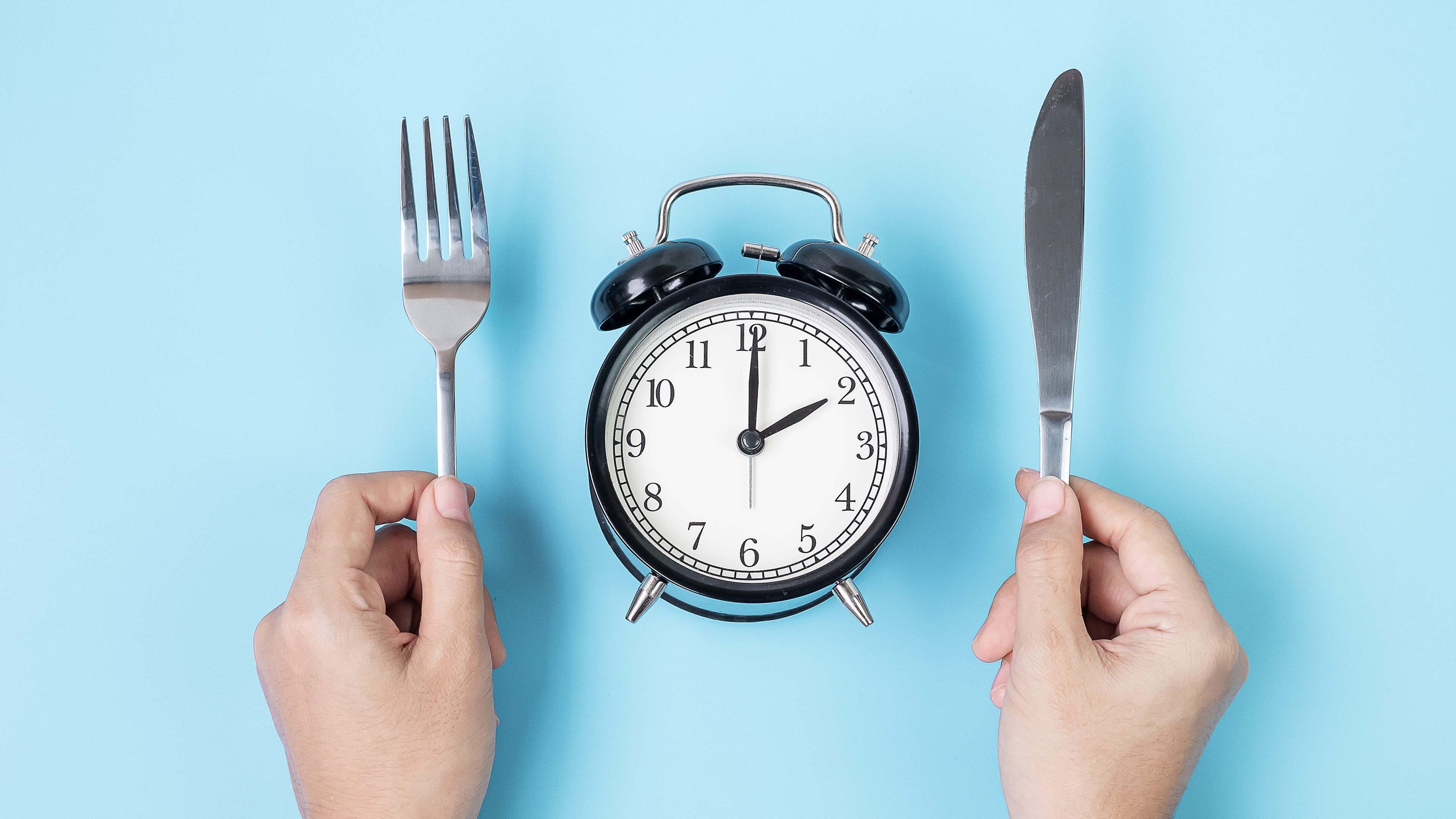 Person holding a knife and fork over an alarm clock